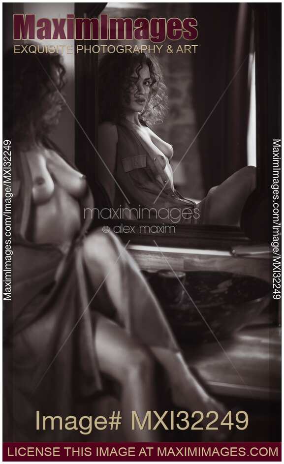 Black and white portrait of a sexy young woman sitting topless by the mirror in unbuttoning dress revealing her breasts