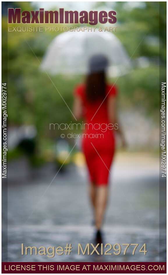 Blurred back of woman in red dress with umbrella walking away in the rain