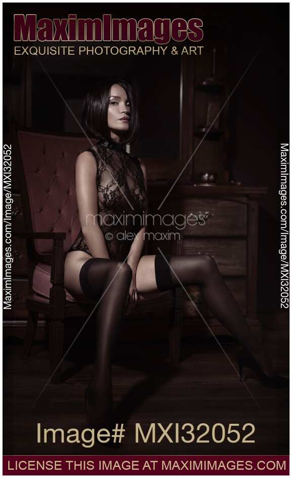 Boudoir portrait of a sexy woman with short hair in black lingerie and stockings sitting in a chair with a bold provocative look