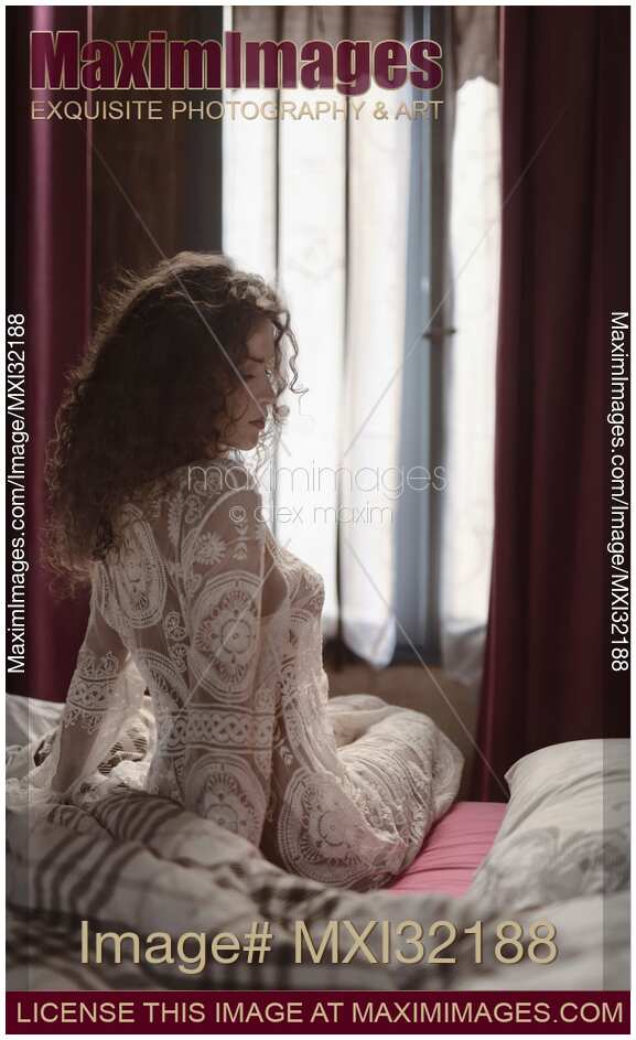Boudoir portrait of beautiful sexy woman sitting in bed just awaken wearing sheer nightgown in morning light