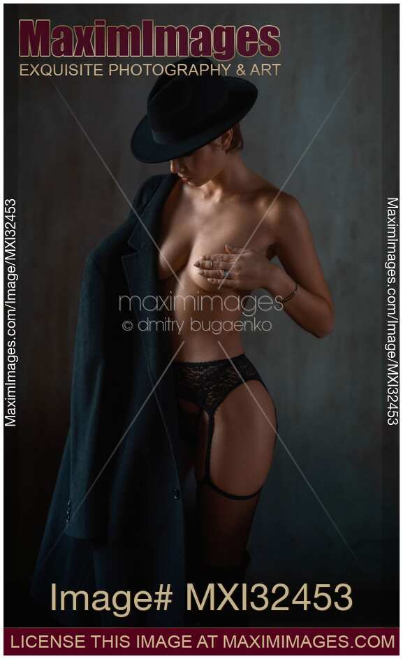 Boudoir portrait of mysterious half naked woman in black hat and lingerie with a coat over her shoulder