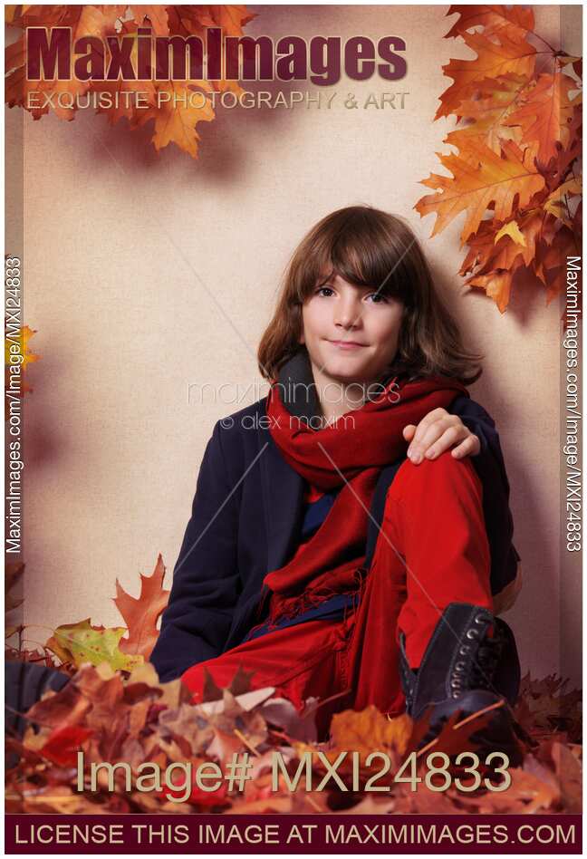 Boy in fall clothes sitting on red autumn leaves