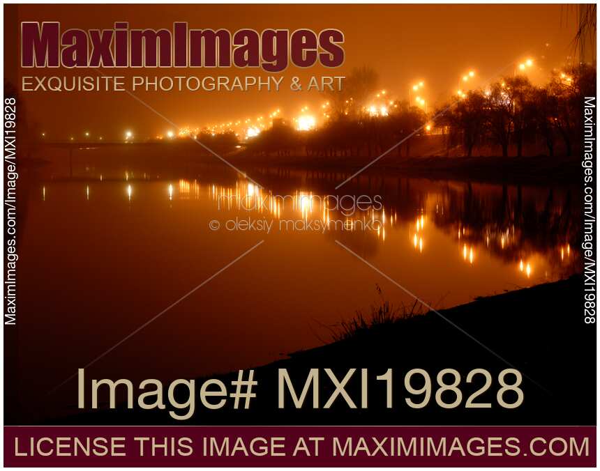 City lights reflecting in river water on foggy night
