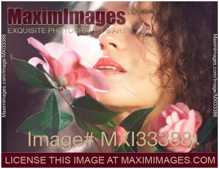 Closeup of a beautiful sensual young woman with red lips smelling pink camellia flowers