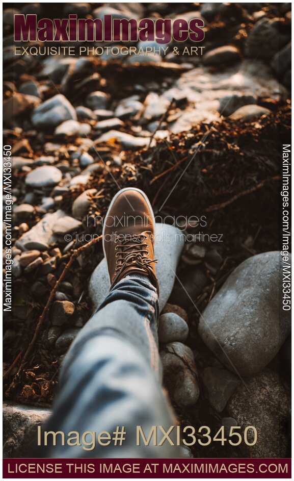 Closeup of a man's leg in brown hiking shoes walking on a pebble beach