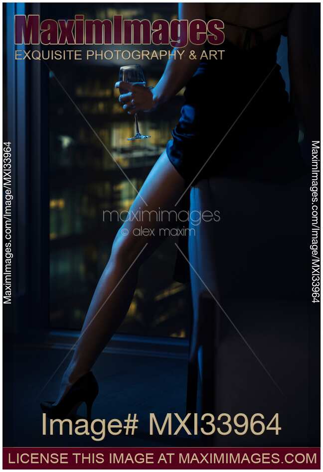 Closeup of a sexy leg in high heel shoes of a woman sitting with a glass of wine by a condo window at night