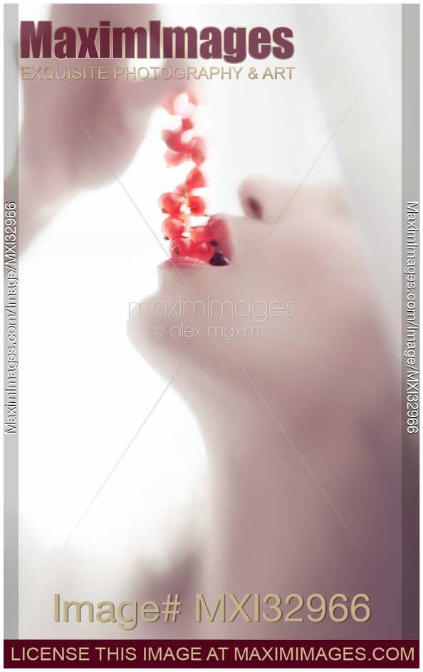 Closeup of a woman taking bright red currants in her sensual mouth with open lips