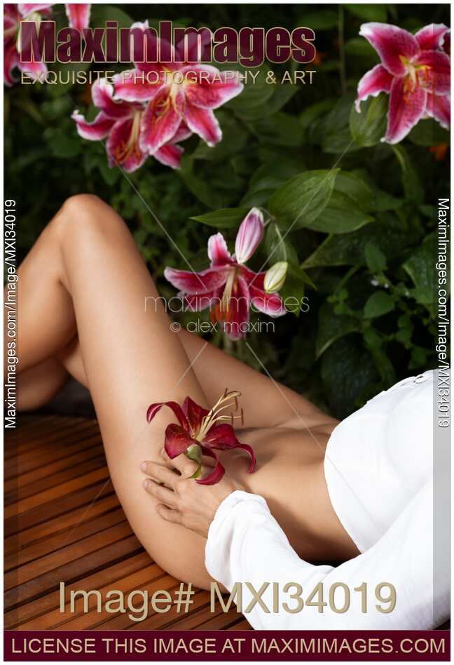 Closeup of half-naked woman body lying on garden bench with pink lily flower in hand