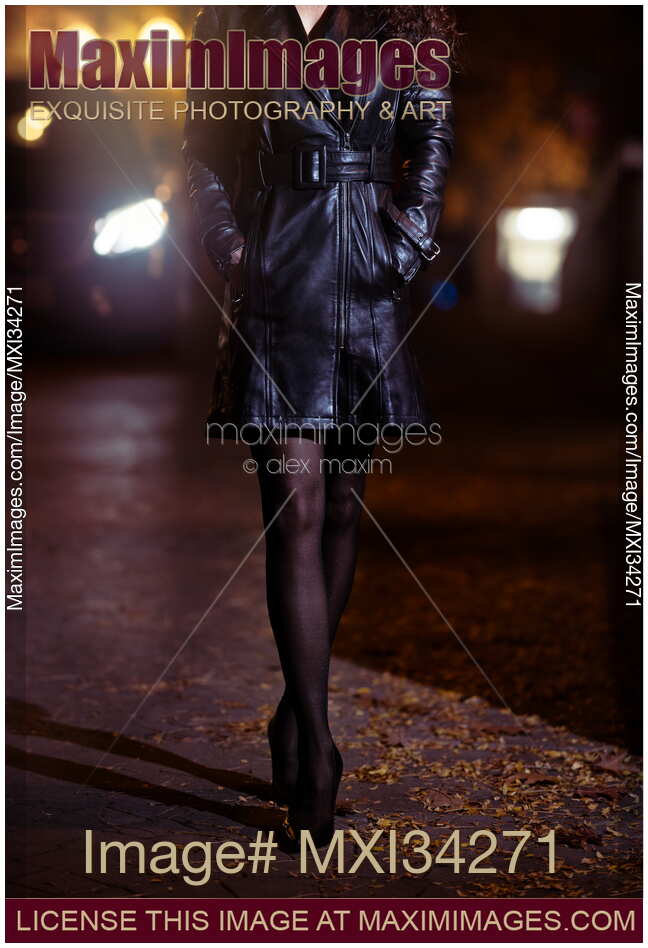 Closeup of legs in black tights of sexy woman in leather coat walking along night city street in car lights