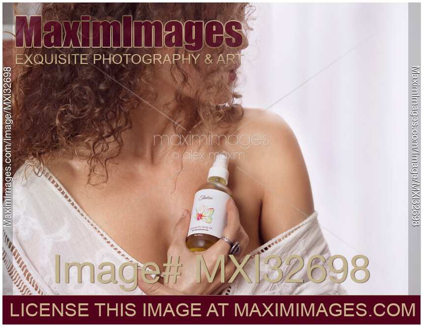 Closeup of woman bare shoulder with a body oil bottle in her hand Skin care concept