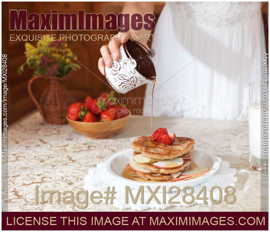 Closeup of young woman pouring maple syrup on pancakes