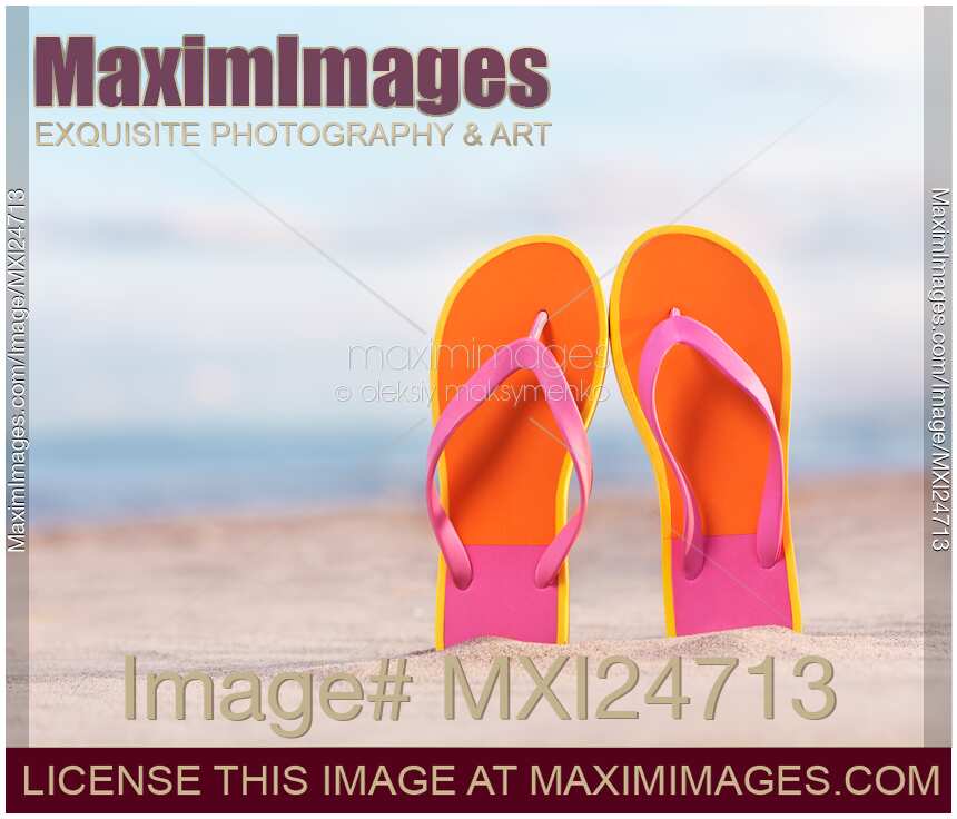 Colorful orange flip flops in sand at the beach