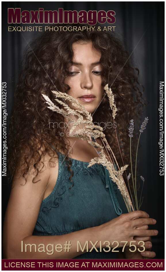 Cute girl with curly hair and expressive big eyes looking down on flowers in her hands