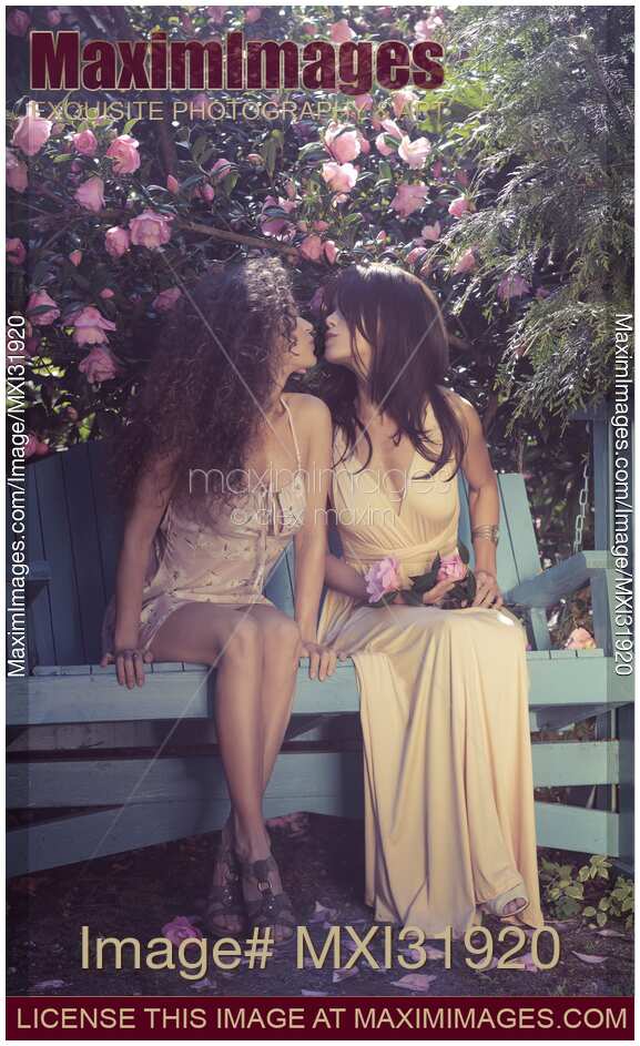 Cute lesbian couple kissing on a bench in a garden