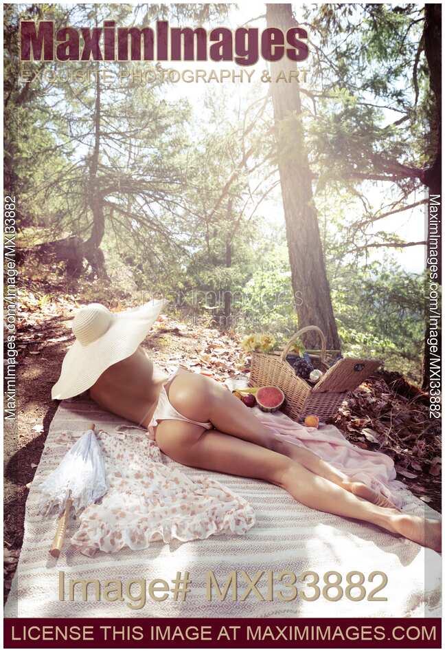 Cute sexy woman in sun hat and underwear relaxing at a picnic in summer nature scenery with view on her back and sexy buttocks