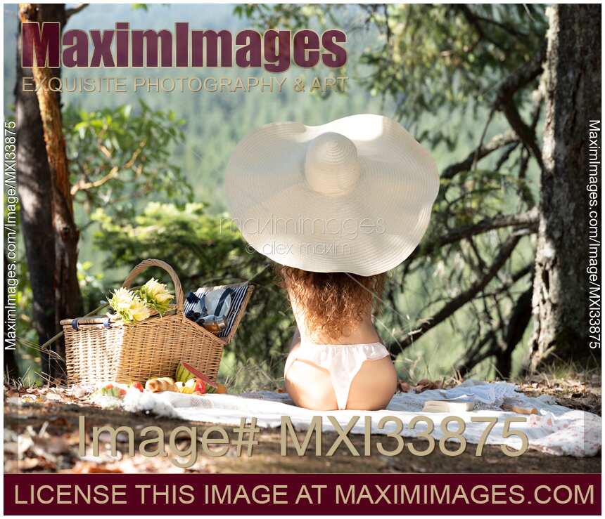 Cute woman in sun hat and underwear relaxing in sunshine at a picnic in summer nature scenery with view on her back