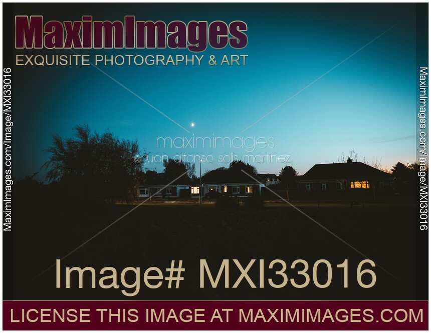 Dark residential houses with lit up windows on a street in dramatic night town scenery