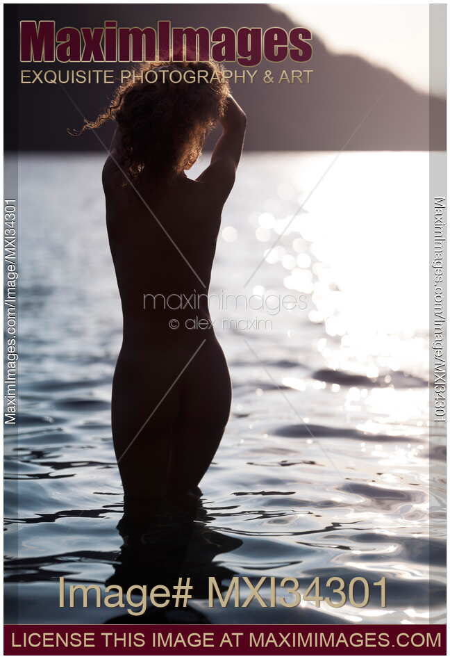 Dark silhouette of a nude woman entering lake water at sunset rear view from behind