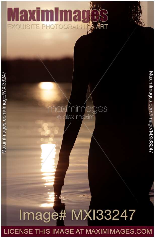 Dark silhouette of a woman walking into the sea at sunset her hand touching the water