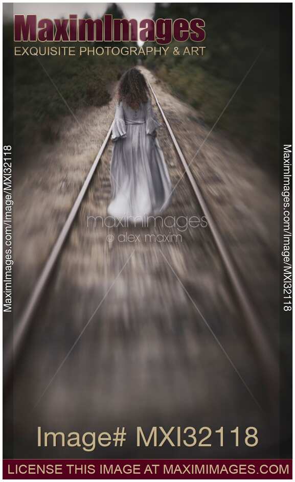 Dramatic concept of a woman in a long dress walking away along railroad tracks