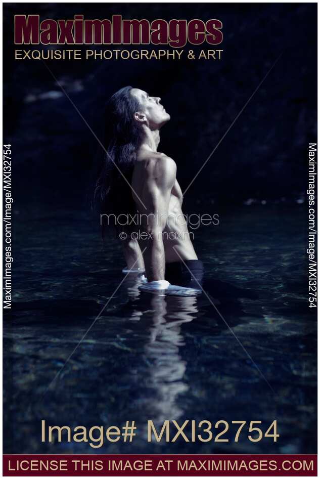 Dramatic portrait of a shirtless man with bare torso standing in water in pants