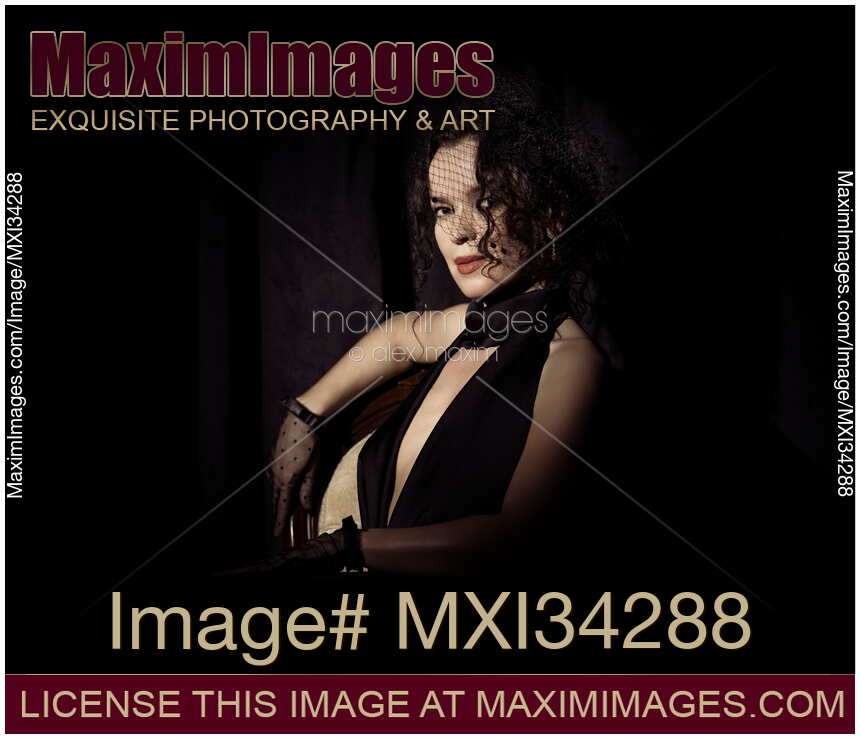 Dramatic portrait of beautiful mysterious femme fatale lady dressed in black wearing veiled hat covering her face