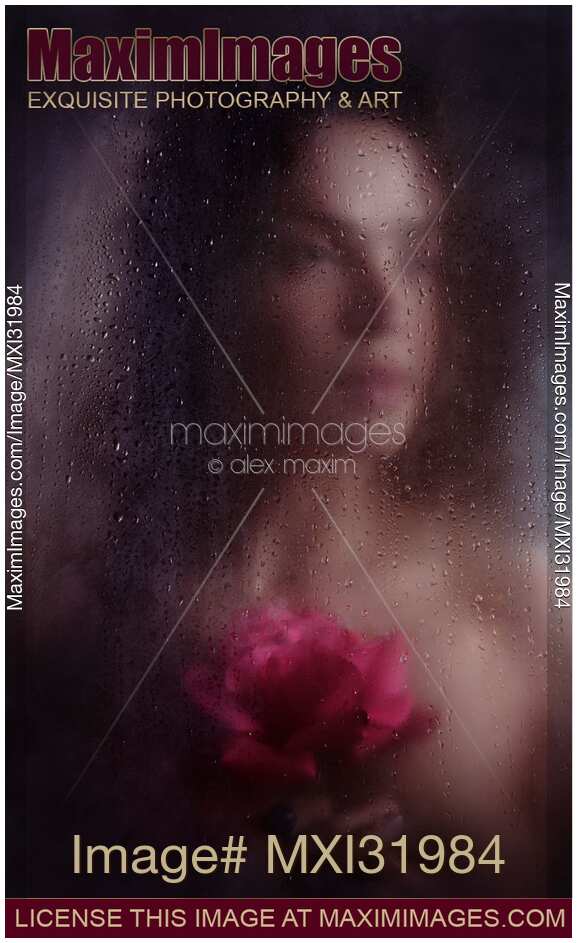 Dream-like romantic portrait of a woman face with a rose behind a hazy wet window glass