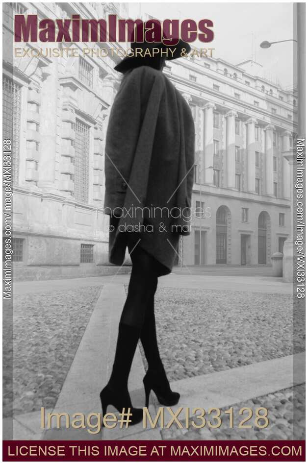 Elegant incognito woman on a city street wearing a fashionable coat, black stockings, high heels and a hat