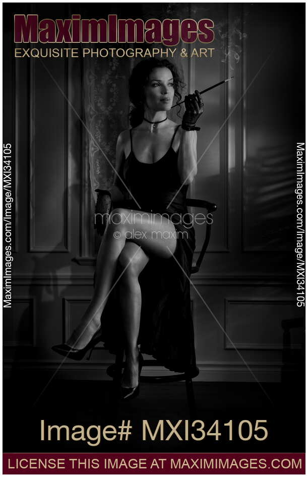 Elegant lady in black dress revealing her sexy legs holding long cigarette holder. Dark noir style portrait.