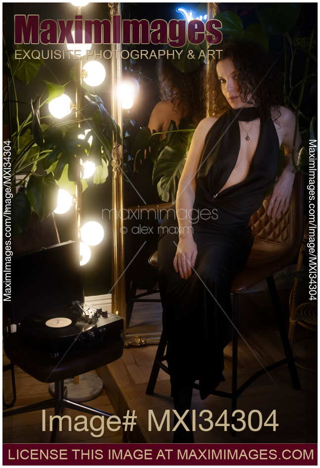 Elegant sexy woman in classy black silk dress sitting on a chair by a vinyl record player