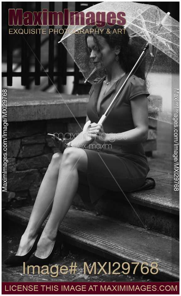 Elegant woman in a dress sitting on the street under umbrella with a phone Black and white