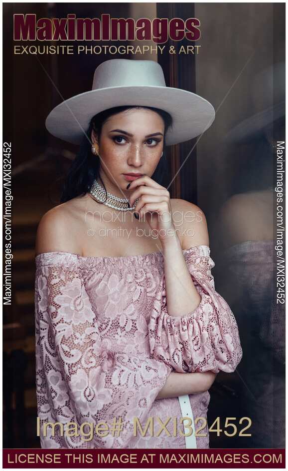 Elegant young woman in pink lace dress and white hat with a thoughtful expression
