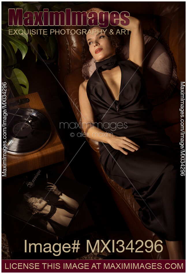 Elegantly dressed classy woman lying relaxing on couch listening to vinyl record in black silk dress