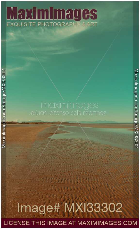 Empty sea beach at low tide in sunrise with wave patterns in the sand under blue sky