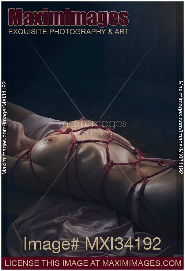 Erotic photograph of nude woman lying down tied up with red Shibari bondage ropes around her sexy naked body