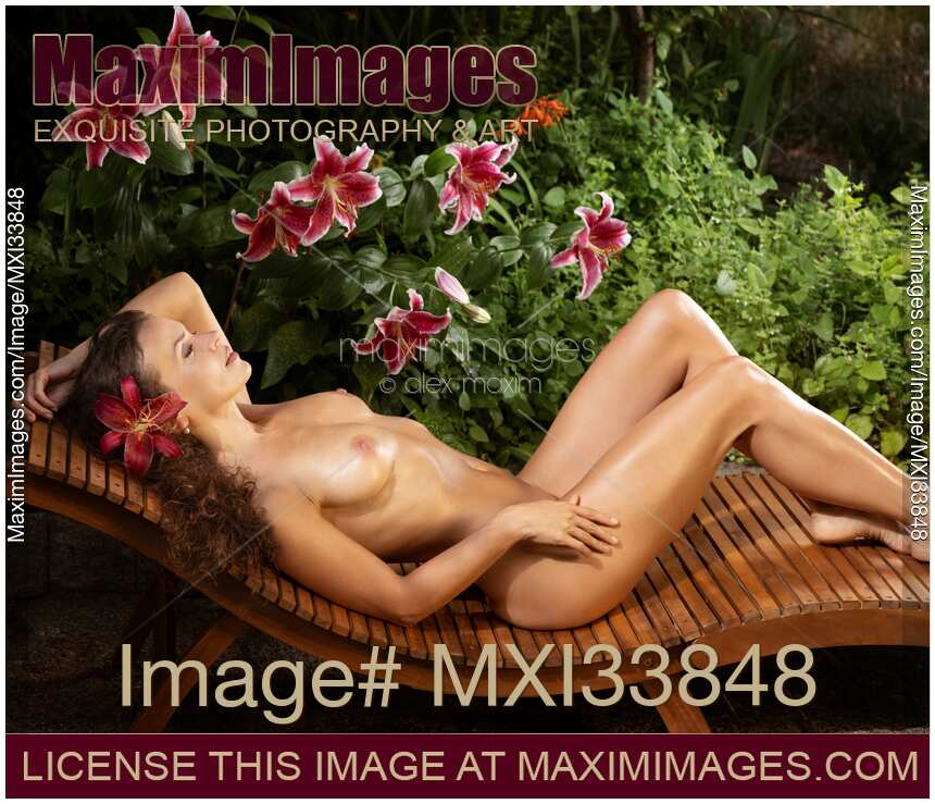 Erotic portrait of a beautiful sexy woman with wet naked sun-tanned body lying on a chaise in tropical lily garden