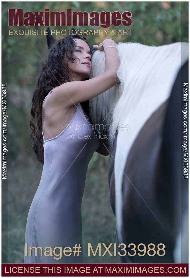 Expressive portrait of a beautiful young woman hugging a black horse with white mane