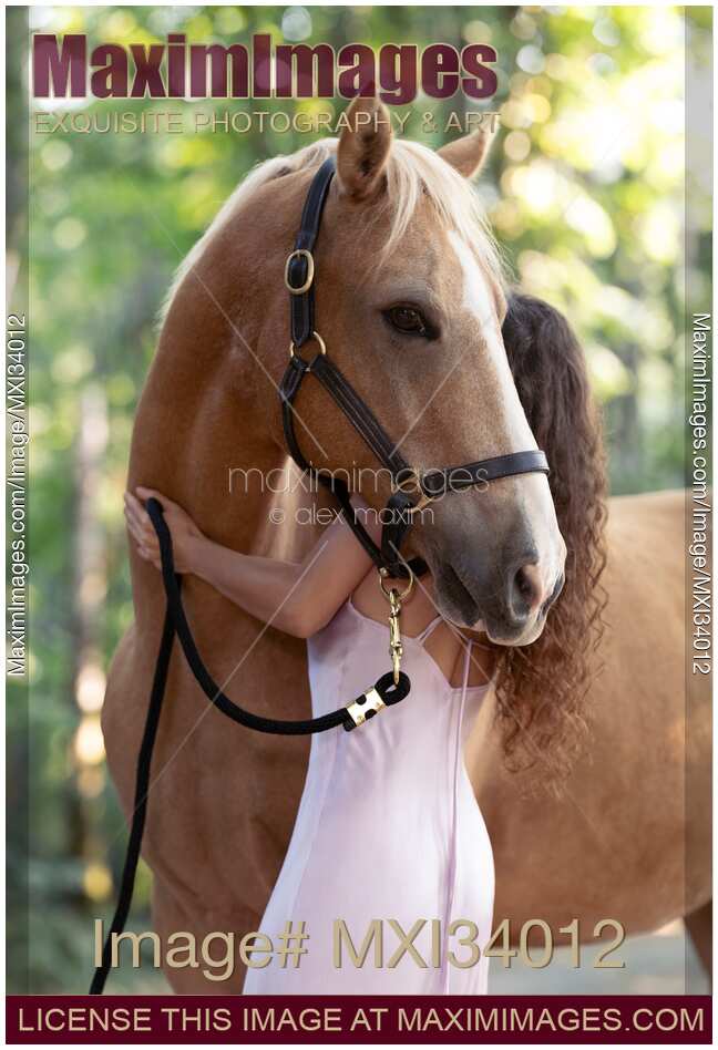 Expressive portrait of a young woman hugging a Palomino horse with white mane in summer nature scenery