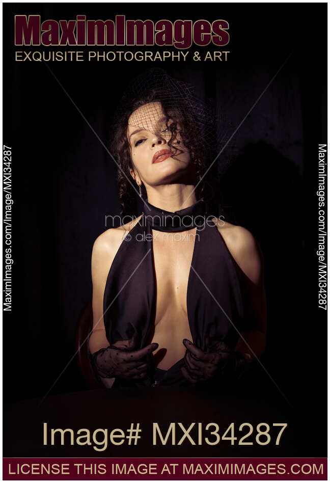 Expressive sensual portrait of beautiful seductive femme fatale lady in black dress and veil exposing her cleavage