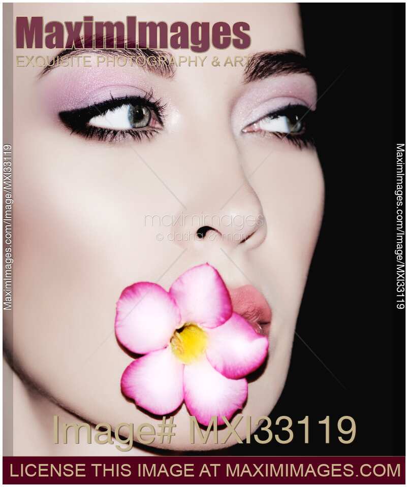 Fashion face portrait of a gorgeous woman with blue eyes and porcelain skin holding a flower in her mouth