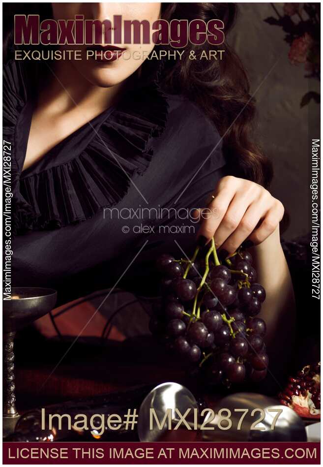 Femme fatale woman with dark lips holding black grapes in her hand