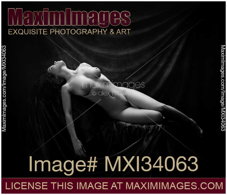 Fine art nude black and white figure portrait of a beautiful woman with sensual voluptuous body lying naked in artist studio on dark background