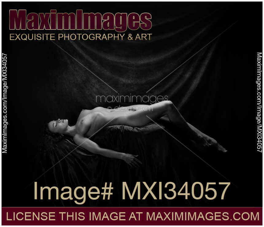 Fine art nude black and white photograph of a beautiful woman lying naked posing in artist studio on dark background