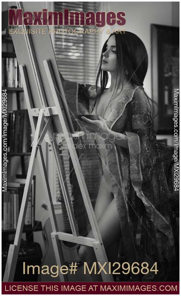 Fine art nude black and white portrait of woman artist painting naked in her home studio on easel