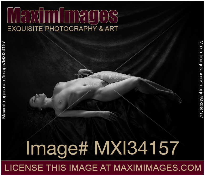 Fine art nude black and white portrait of woman lying in graceful pose in artist studio revealing sensual curves of her naked body