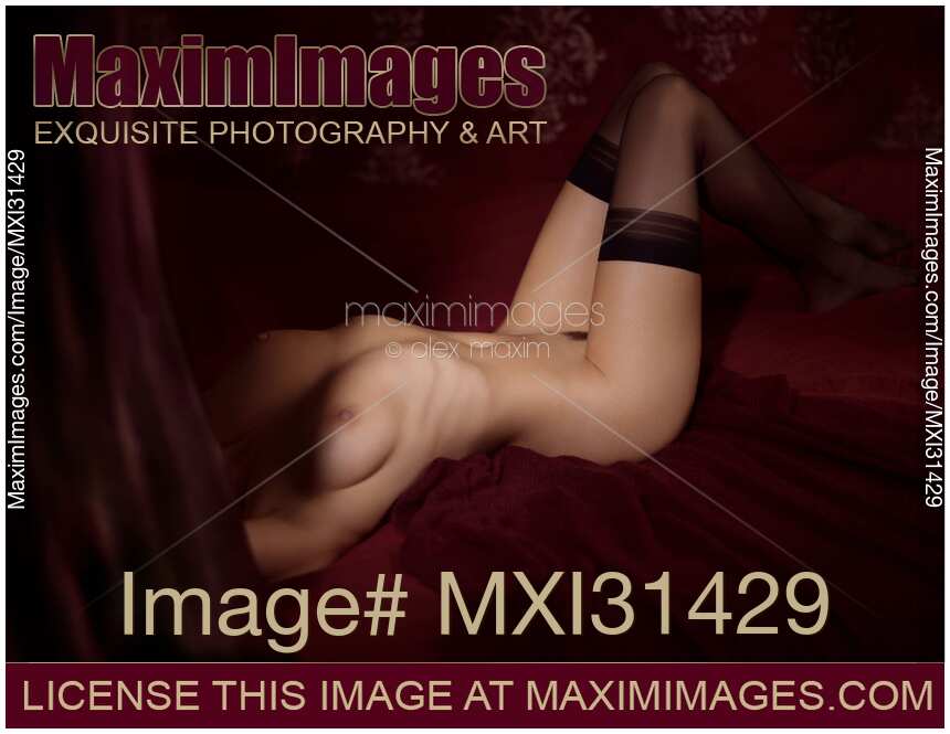 Fine art nude body figure of a woman in stockings lying down in bed naked obscured by a curtain