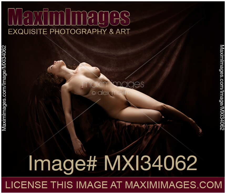 Fine art nude figure portrait of a beautiful woman with sensual voluptuous body lying naked in artist studio on dark background