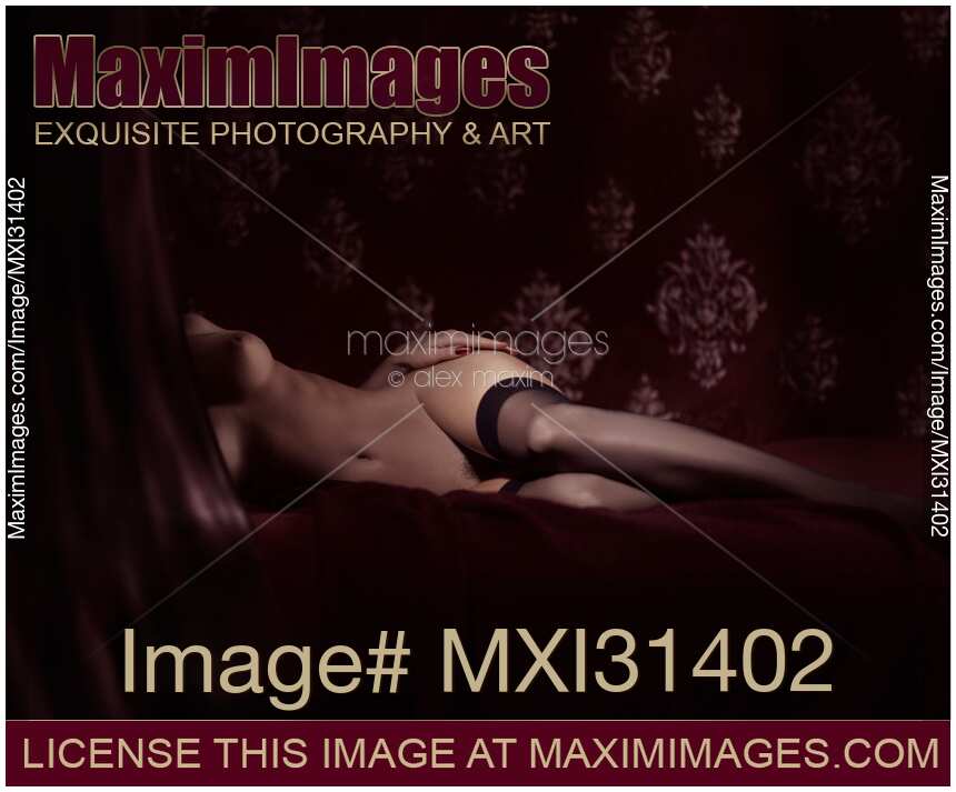 Fine art nude photo a woman in black stockings lying naked on bed with her hand on her hip