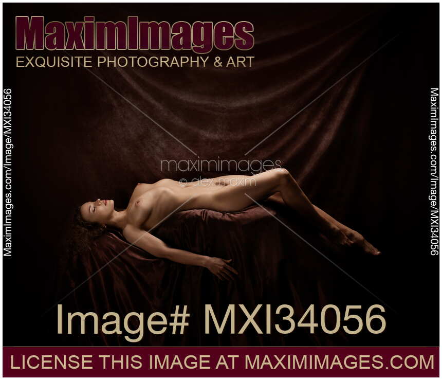 Fine art nude photograph of a beautiful woman lying naked posing in artist studio on dark background
