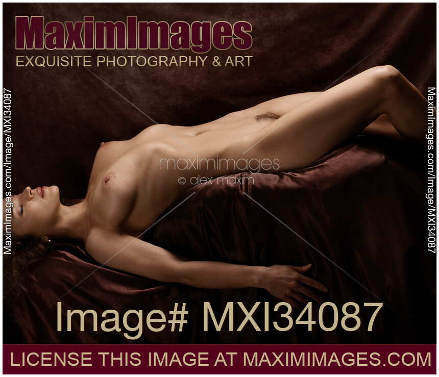 Fine art nude photograph of a beautiful young woman lying naked in a sensual pose with her sensual body exposed and her breast arching upwards